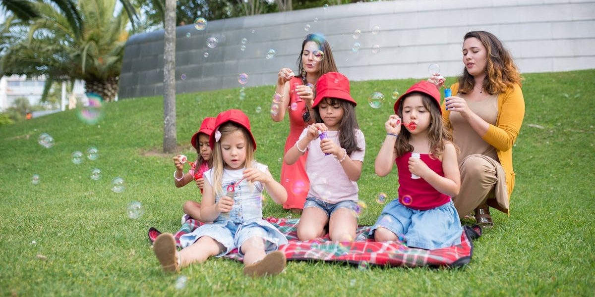 Group of children and adults blowing bubbles in a sunny park setting.