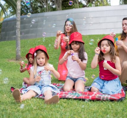Group of children and adults blowing bubbles in a sunny park setting.