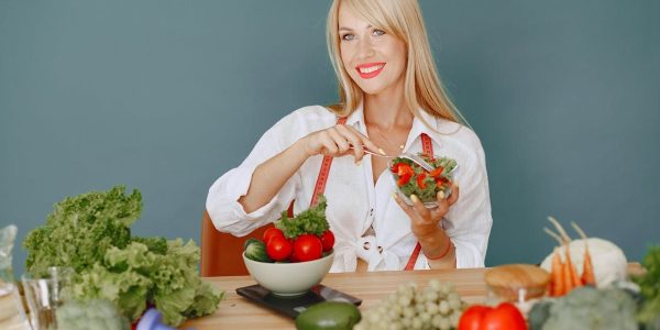 Blonde woman enjoying a fresh salad surrounded by vegetables, promoting healthy eating.